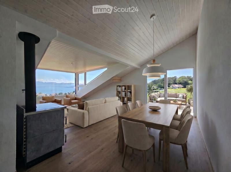Modern living room with large windows offering a scenic view, featuring a sofa, dining table, chairs, bookshelf, and armchairs.
