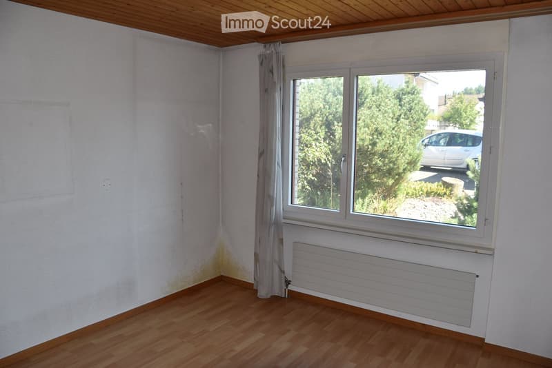 Empty room with wooden flooring, white walls, a window with a curtain, and a radiator below the window.