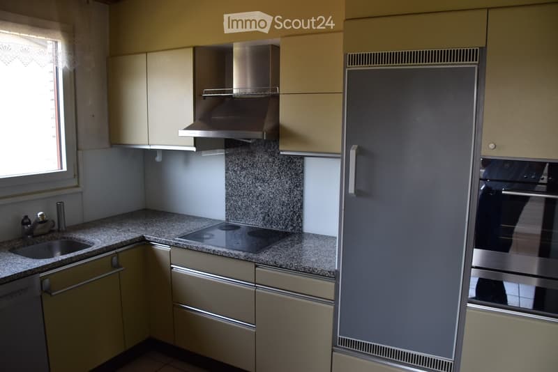 Modern kitchen with light-colored cabinets, granite countertops, stainless steel appliances including a stove, oven, and refrigerator, and a window with a curtain.