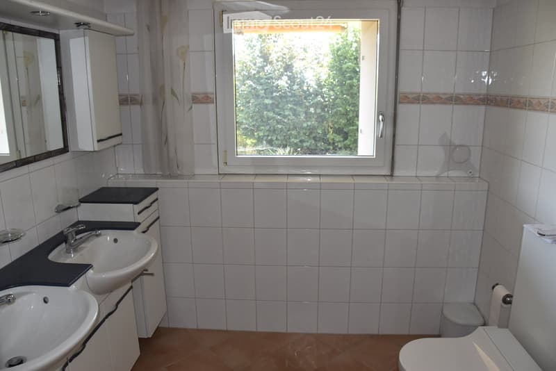 Bathroom with two sinks, a toilet, a mirror, and a window with a view of greenery outside.