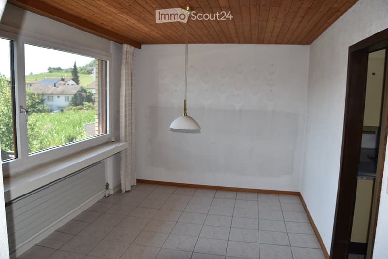 Empty room with tiled floor, white walls, large window with view, radiator, and a hanging light fixture.