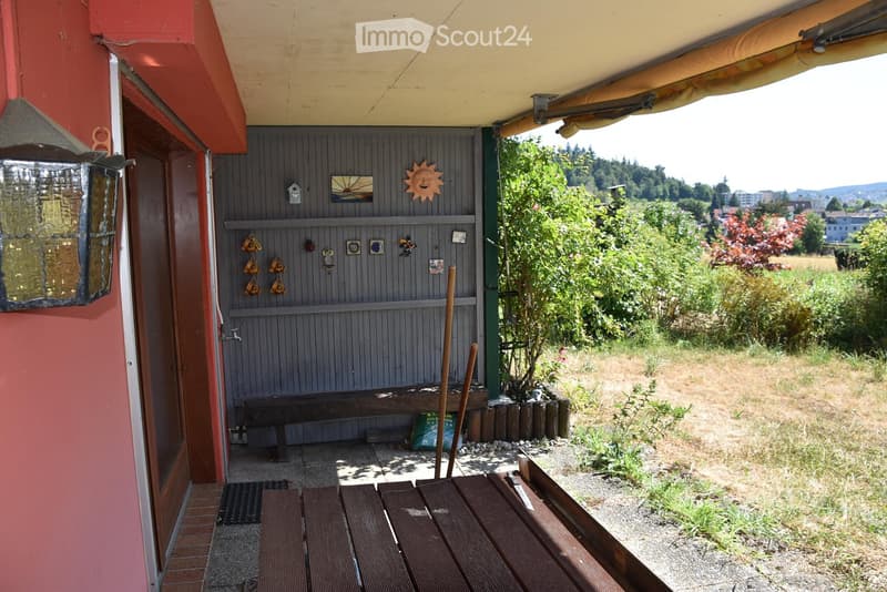 Outdoor area with wooden bench, small storage shed, and decorative items on the wall. The area is surrounded by greenery and has a view of the countryside.