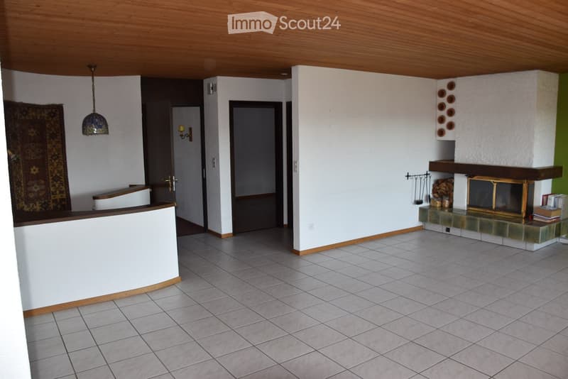 Open living space with tiled floor, white walls, wooden ceiling, fireplace with decorative items, and a rug on the left side.