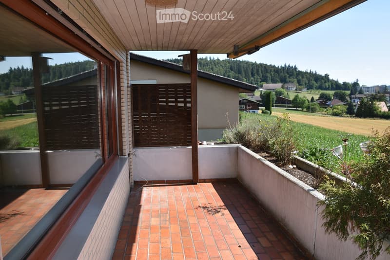Balcony with brick tiles, wooden ceiling, and a view of a rural landscape with fields and trees.