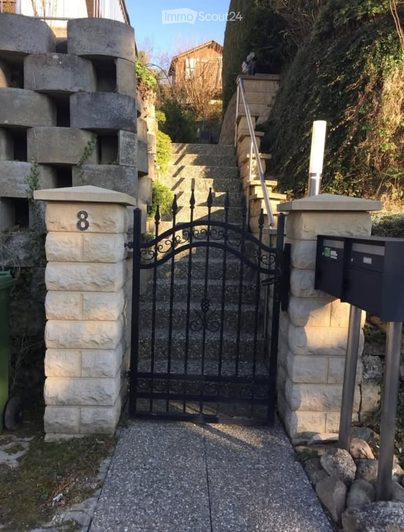 Stone entrance pillars, black wrought iron gate, stone walkway, metal handrails, stone steps, mailboxes on right, number 8 on left pillar.