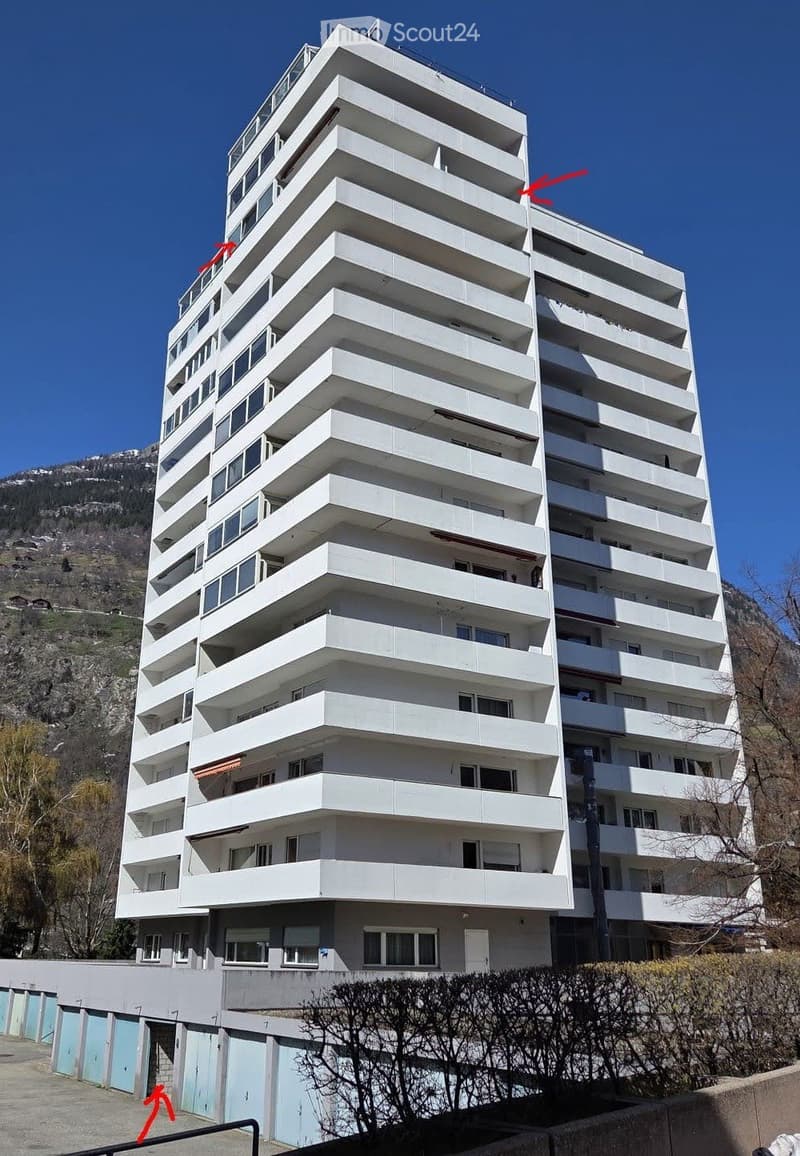 Building. Modern multi-story apartment building with white balconies and large windows, set against a mountainous backdrop.