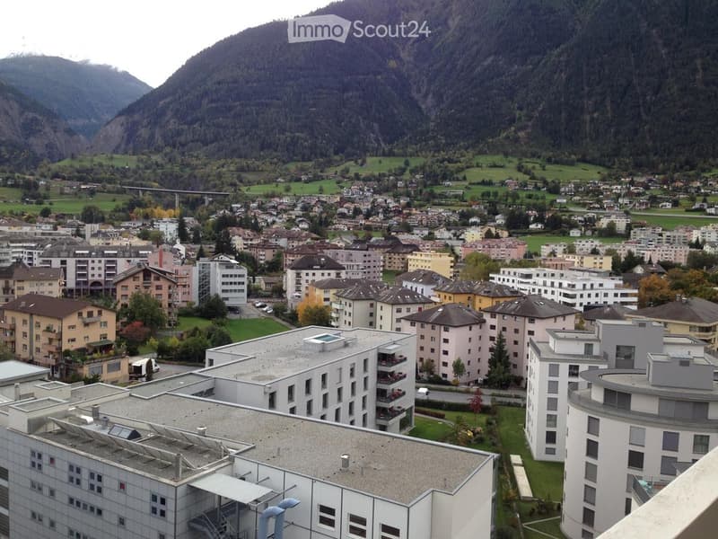 Building. Aerial view of a town nestled in a valley surrounded by mountains, featuring multiple residential and commercial buildings with varied architectural styles and colors.