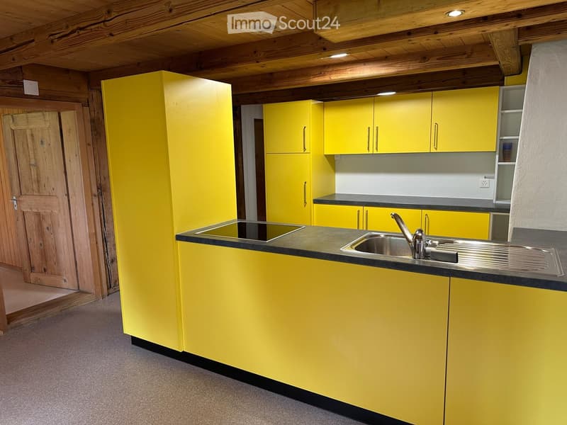 Bright yellow kitchen with modern cabinets, a stainless steel sink, and a countertop, featuring wooden beams on the ceiling and a wooden door in the background.