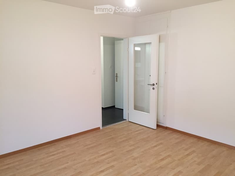 Empty room with light wooden flooring, white walls, and a white door leading to another room.