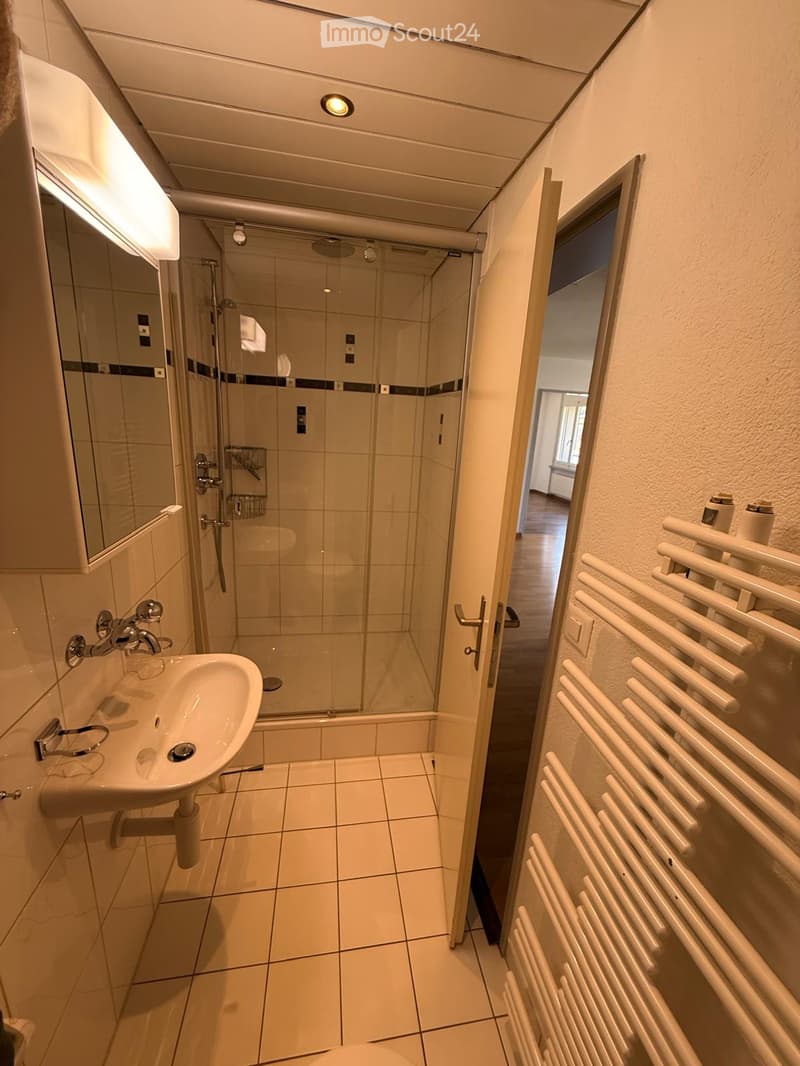 Modern bathroom with a white tiled floor, a sink with a chrome faucet, a glass-enclosed shower, a mirror cabinet, and a white radiator.