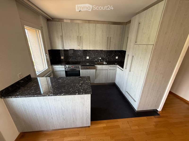 Modern kitchen with light wood cabinets, granite countertops, and stainless steel appliances including an oven, sink, and dishwasher.