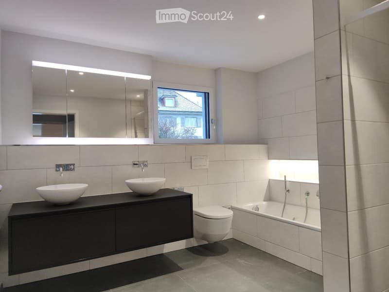 Modern bathroom with two sinks, a bathtub, a toilet, a large mirror, and built-in cabinets.
