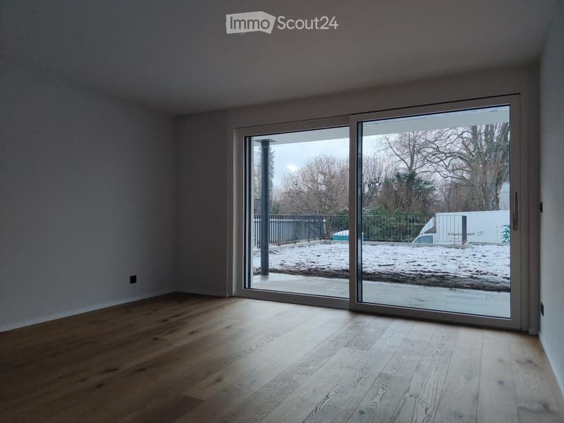 Empty room with wooden flooring and large sliding glass doors leading to an outdoor area covered in snow.