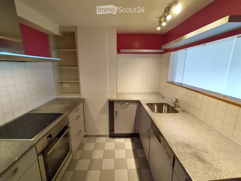 Modern kitchen with white cabinets, granite countertops, stainless steel sink, and built-in oven. Features include a window, track lighting, and a shelf unit.