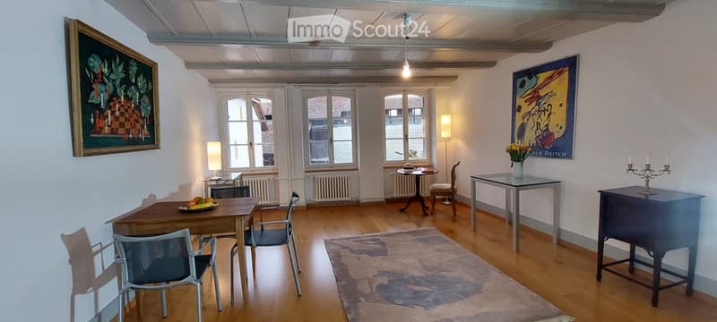 Bright, wooden-floored room with large windows, dining table with chairs, side tables, artwork, and decorative items.