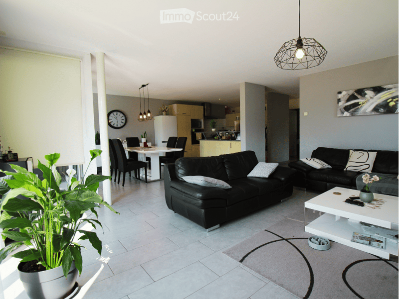 Modern living and dining area with a black leather sofa, white coffee table, dining table with chairs, potted plants, and a clock on the wall.