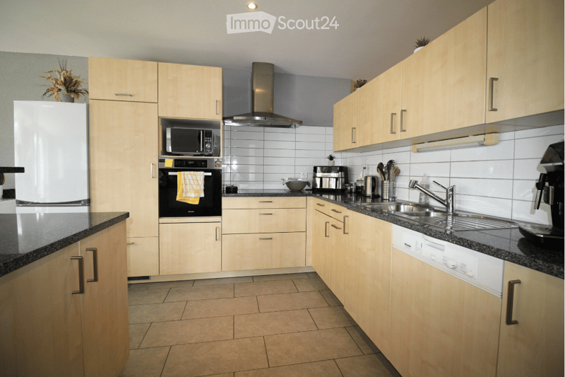 Modern kitchen with light wood cabinets, stainless steel appliances, granite countertops, and tiled flooring.