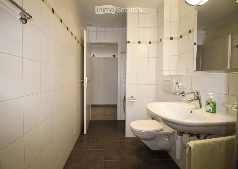 Modern bathroom with white tiled walls, a sink with a chrome faucet, a toilet, a mirror, and a towel on a rack.