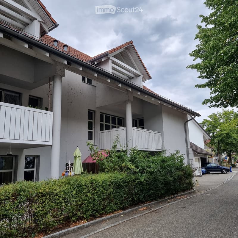 Two-story residential building with white exterior, multiple windows, balconies, and a well-maintained garden area.