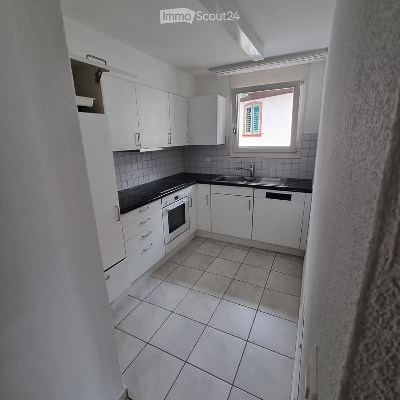 Modern kitchen with white cabinets, tiled floor, black countertop, and built-in appliances including an oven and sink.