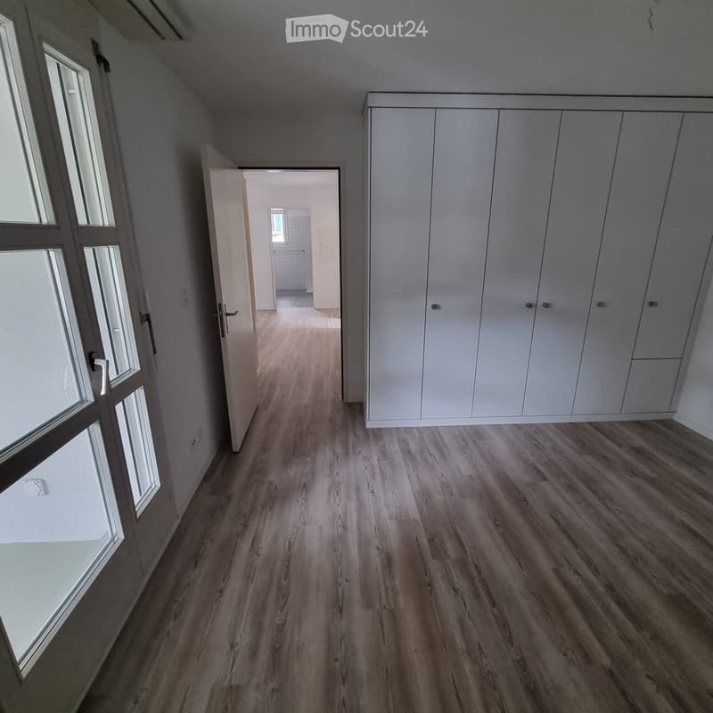 Empty hallway with wooden flooring, white walls, built-in white closet, and a door leading to another room.