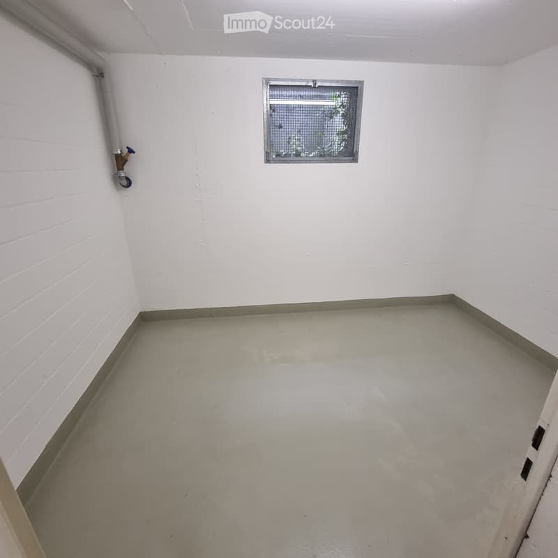 Empty room with white brick walls, concrete floor, and a small window with a metal frame. A water tap is visible on the left wall.