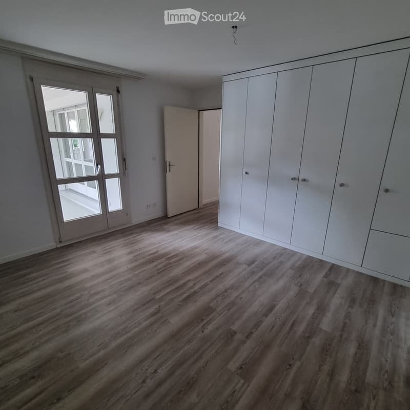 Empty room with wooden flooring, white walls, large sliding glass door, and built-in white wardrobe.