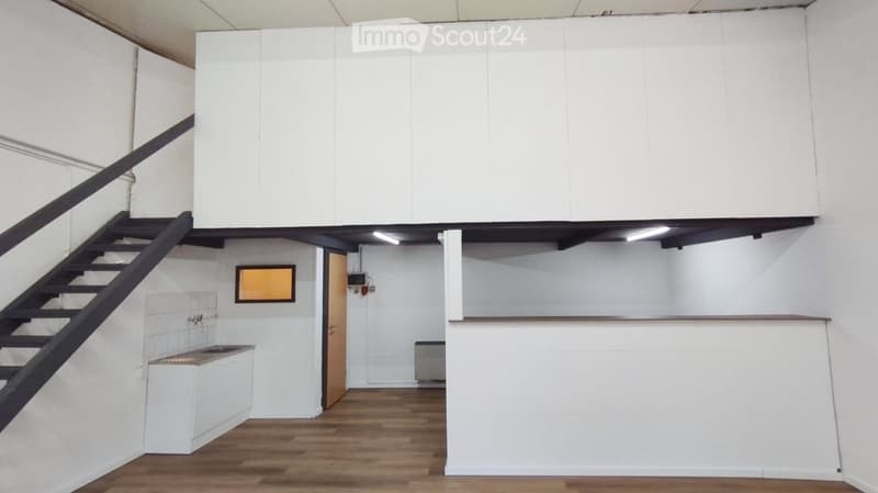 Empty room with white walls, wooden floor, staircase leading to a loft area, and a small sink area.