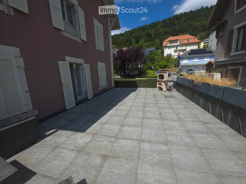 Spacious balcony with tiled flooring, low railing, and a small outdoor seating area with a table and chairs.