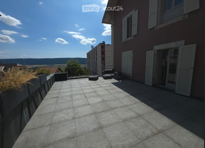 Balcony with tiled floor, metal railing, and a few stools and a small table.