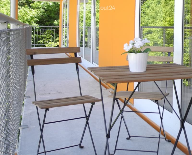 Balcony with a small wooden table, two folding chairs, and a white flower pot on the table.