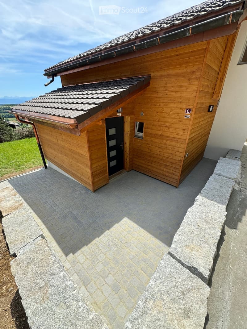 A small wooden building with a tiled roof, a stone-paved entrance area, and a raised ground floor.