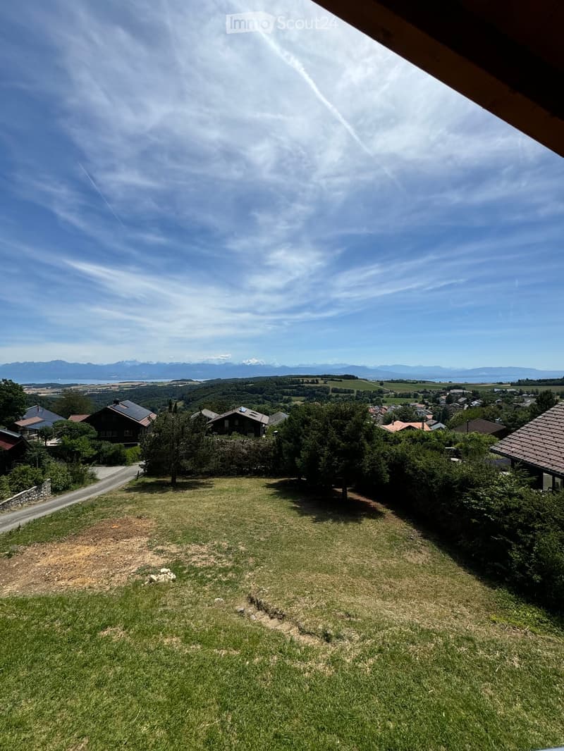 Panoramic view of a rural landscape with houses, trees, and distant mountains under a clear blue sky.