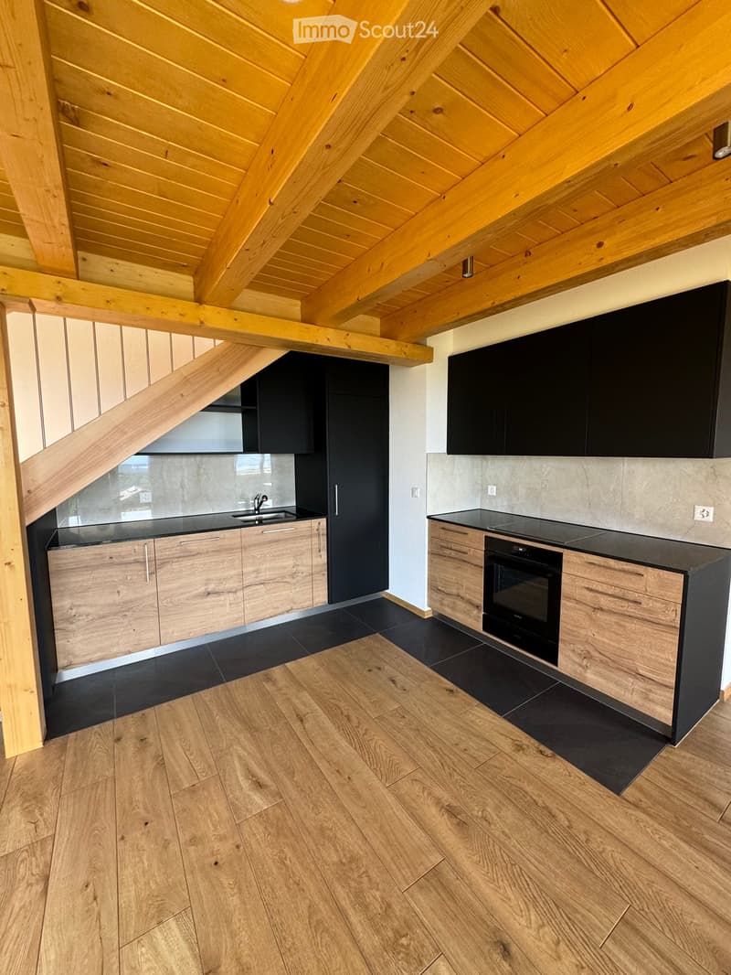 Modern kitchen with wooden beams, black countertops, and stainless steel appliances. Features include a sink, oven, and wooden cabinets.
