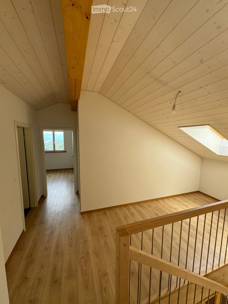 Wooden staircase with a wooden railing, light-colored walls, and a skylight at the top, leading to a room with a window showing a scenic view.