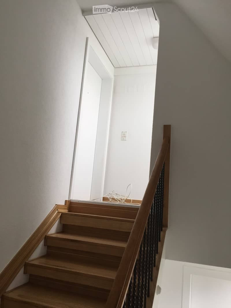 Wooden staircase with a handrail and open landing leading to an upper level, featuring white walls and a skylight above.