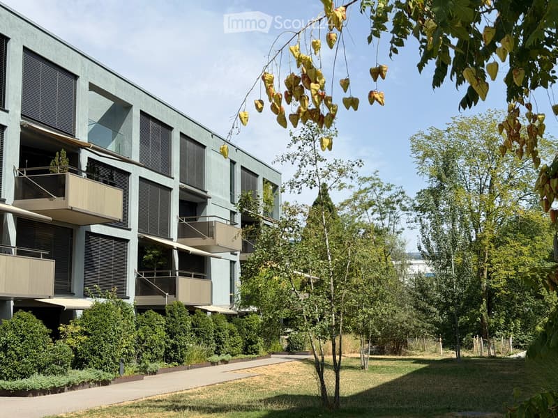Modern multi-story building with balconies, surrounded by trees and greenery.
