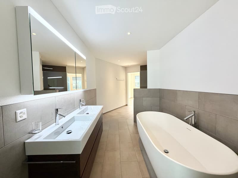 Modern bathroom with double sink, bathtub, large mirror, and sleek fixtures.