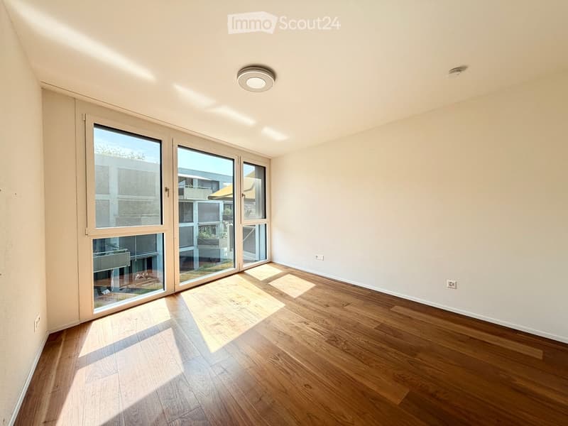 Empty room with wooden flooring, large sliding glass doors, and natural light streaming in.