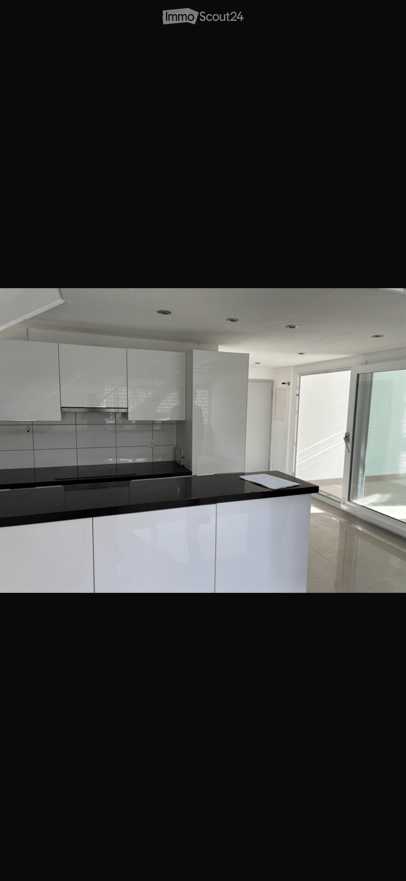 Modern kitchen with white cabinets, black countertop, and a large window providing natural light.