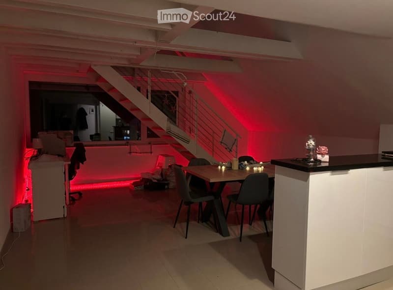 Modern open-plan living and dining area with a staircase leading to an upper level, featuring a dining table with chairs, a kitchen counter, and ambient lighting.