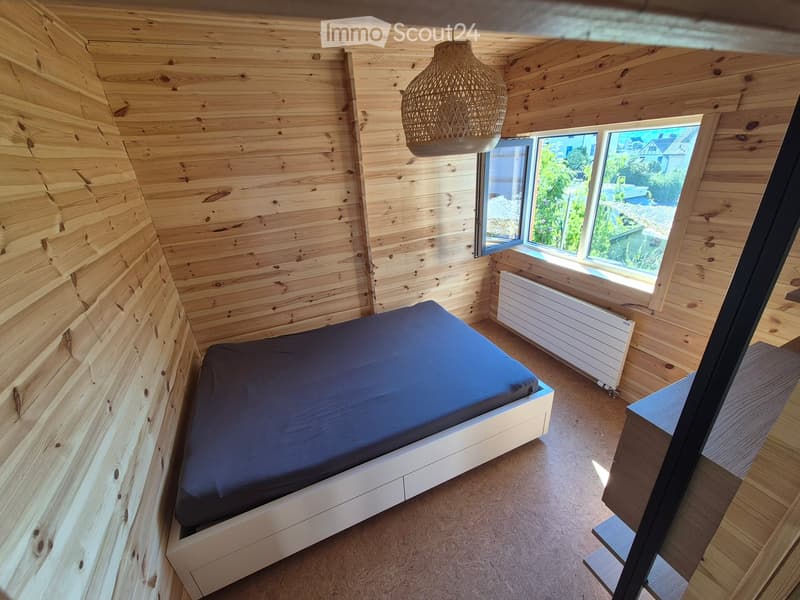 Cozy bedroom with wooden walls and floor, a single bed with blue bedding, a white radiator, and a wicker pendant light hanging from the ceiling.