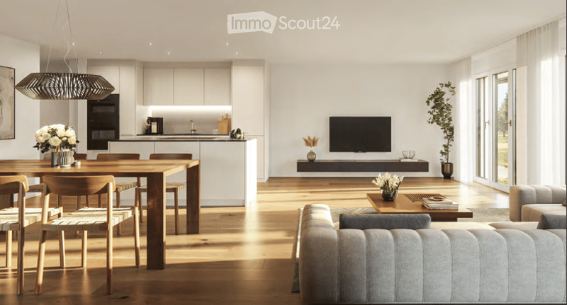 Open-plan living and dining area with modern furniture, including a grey sofa, coffee table, wooden dining table with chairs, and a flat-screen TV on a wall-mounted stand. The kitchen features sleek white cabinets and a pendant light. The space is bright