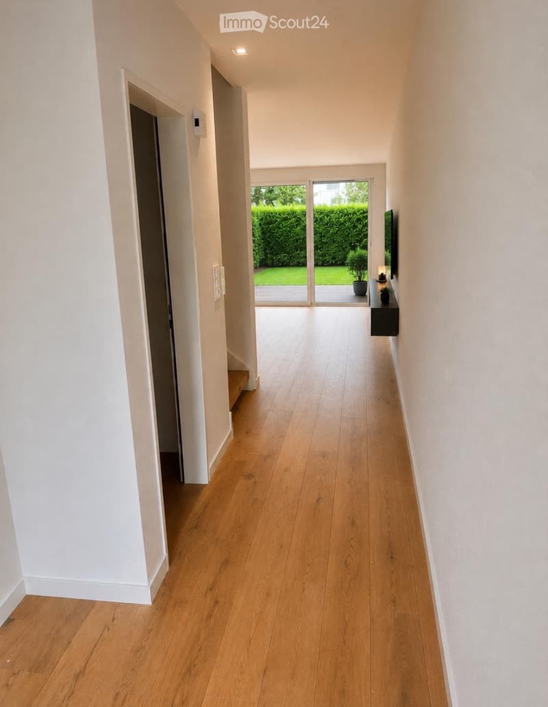 Bright hallway with light wooden flooring, white walls, and a sliding glass door leading to a green outdoor area.
