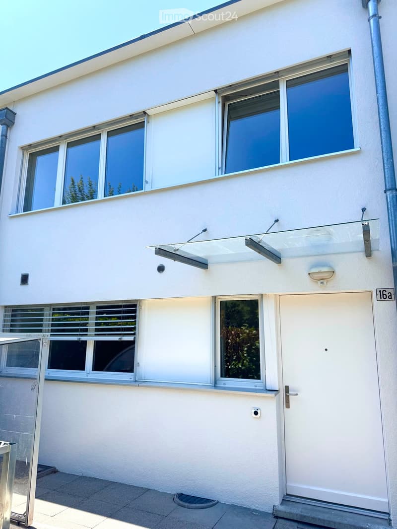 Modern two-story building with white exterior, large windows, and a glass canopy over the entrance.