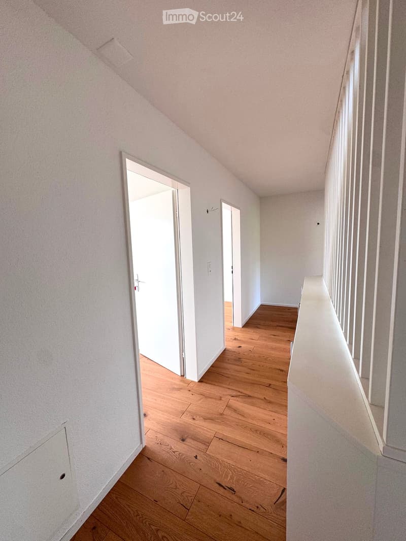 Empty hallway with wooden flooring, white walls, and two open doors leading to other rooms.