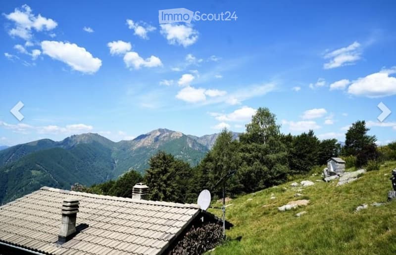 A scenic mountain view with a small stone house and a satellite dish on a grassy slope.