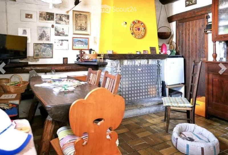 A cozy dining area with a wooden table, chairs, a refrigerator, and a television. The room features a bright yellow accent wall, a stone fireplace, and various decorative items including picture frames and a dog bed.