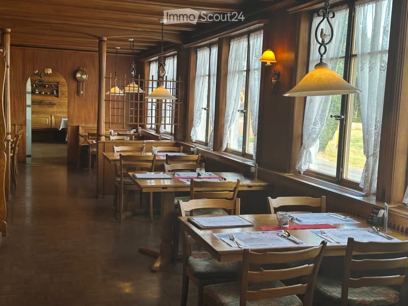 Cozy restaurant interior with wooden tables, chairs, menus, and cutlery, large windows with curtains, and warm lighting.
