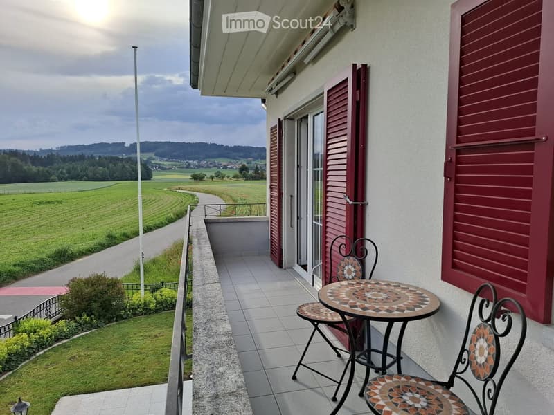 Balcony with a table and two chairs, overlooking a scenic countryside view with fields and trees.